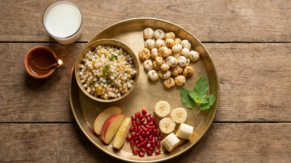 A fasting meal on a brass plate: sabudana khichdi, makhana, fruit and tulsi leaves, with milk and a diya