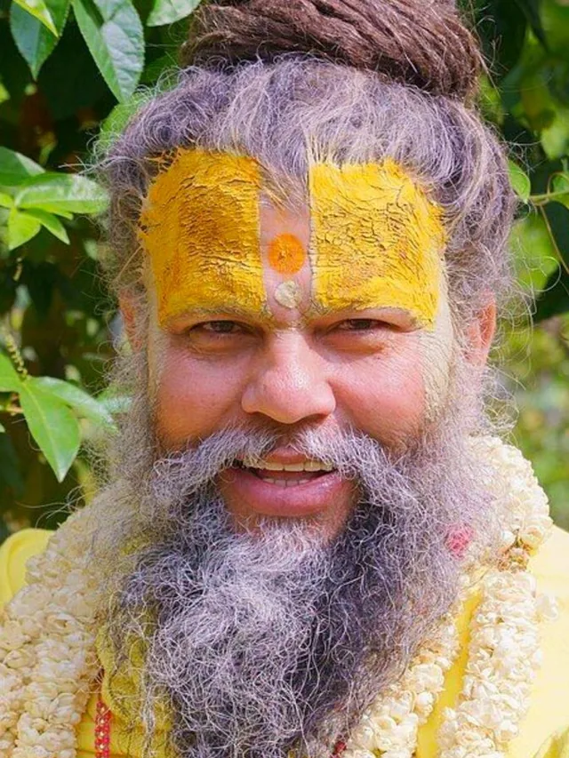 Premanand Ji Maharaj against a green leafy backdrop at Shri Hit Radha Keli Kunj, Vrindavan