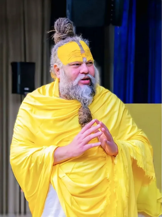 Premanand Ji Maharaj with hands folded before a pale backdrop at Shri Hit Radha Keli Kunj, Vrindavan