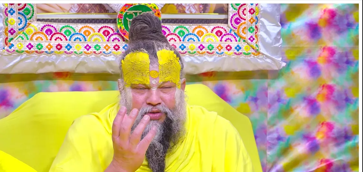 Premanand Ji Maharaj seated before a brightly patterned backdrop