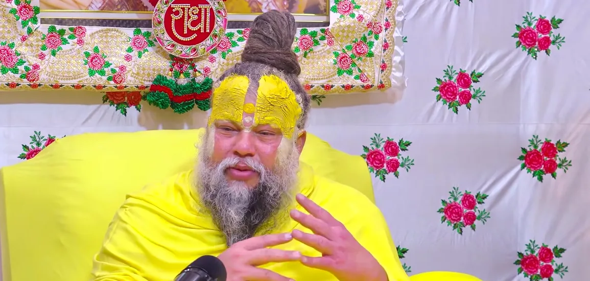 Premanand Ji Maharaj gesturing during satsang, floral backdrop