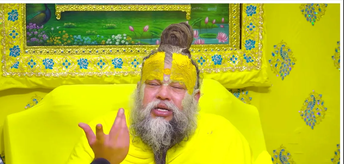Premanand Ji Maharaj gesturing before a green and gold backdrop