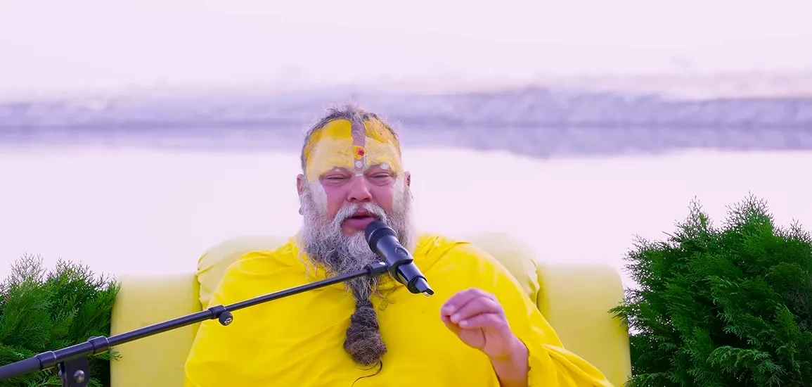 Premanand Ji Maharaj seated outdoors for satsang with the water behind