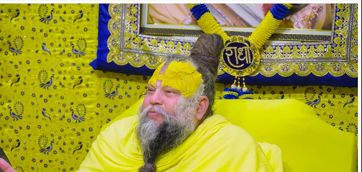 Premanand Ji Maharaj seated on his asan before a gold and blue backdrop