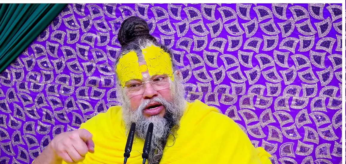 Premanand Ji Maharaj speaking during satsang before a purple backdrop