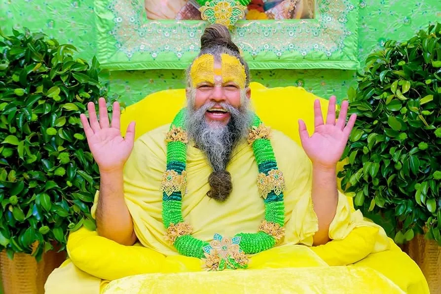 Premanand Ji Maharaj seated on his asan with raised hands, blessing devotees during satsang at Shri Hit Radha Keli Kunj, Vrindavan